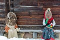 Dolls in MeteÃâ i mumming masks and costumes sitting in a bench near an old wooden house